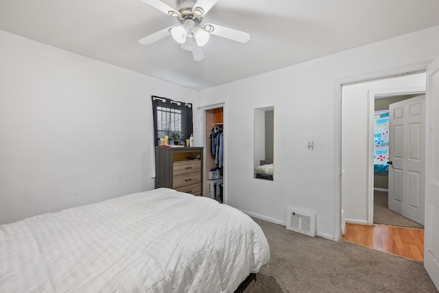 carpeted bedroom with a ceiling fan, visible vents, baseboards, a closet, and a walk in closet