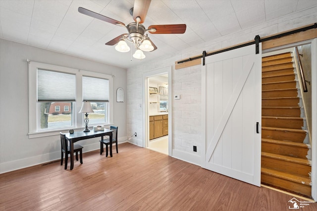 office area featuring baseboards, ceiling fan, light wood finished floors, and a barn door