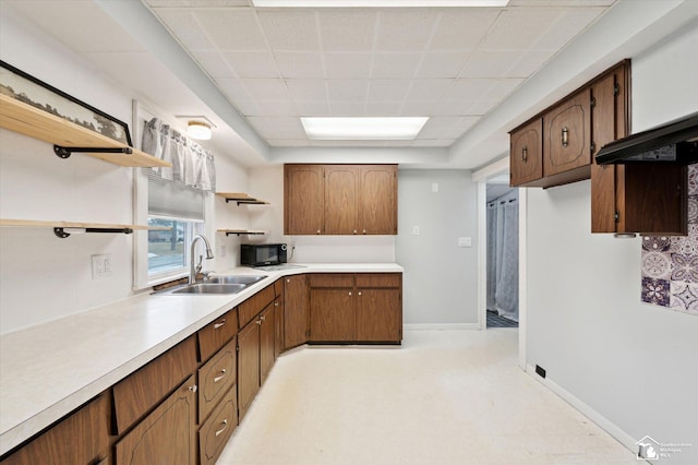 kitchen featuring baseboards, light countertops, black microwave, open shelves, and a sink