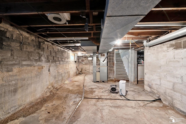 unfinished basement featuring heating unit and stairway