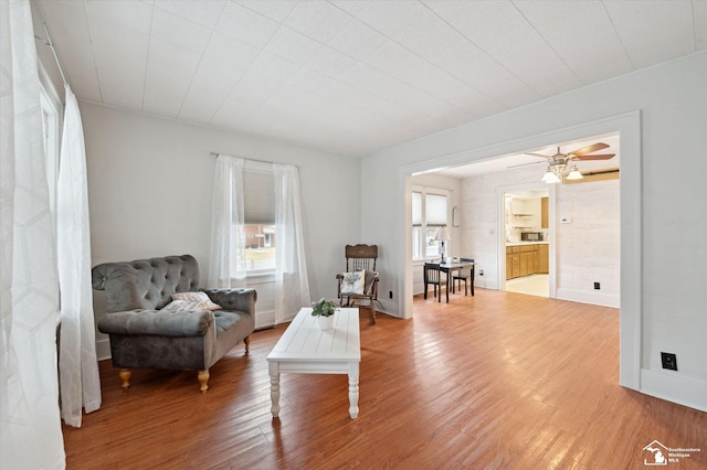 living area with ceiling fan, light wood-style flooring, and baseboards