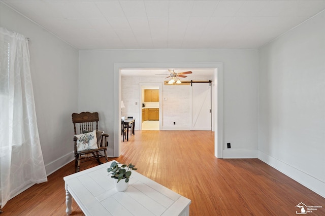 sitting room with baseboards, a barn door, a ceiling fan, and light wood-style floors