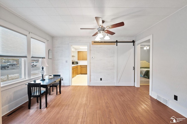 interior space featuring light wood-style floors, a barn door, visible vents, and ceiling fan