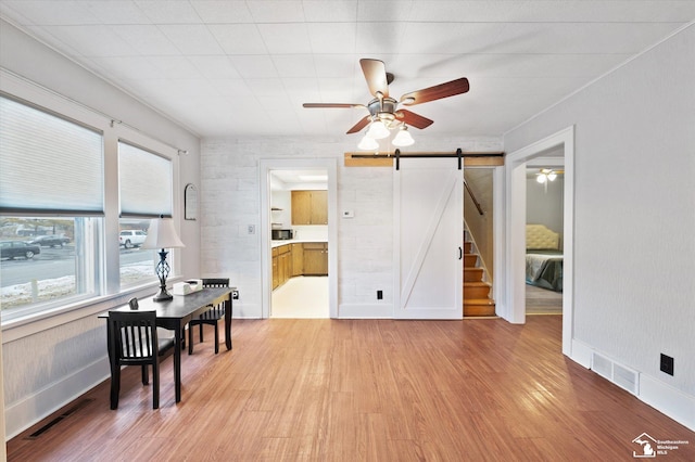 interior space with light wood finished floors, a barn door, visible vents, and ceiling fan