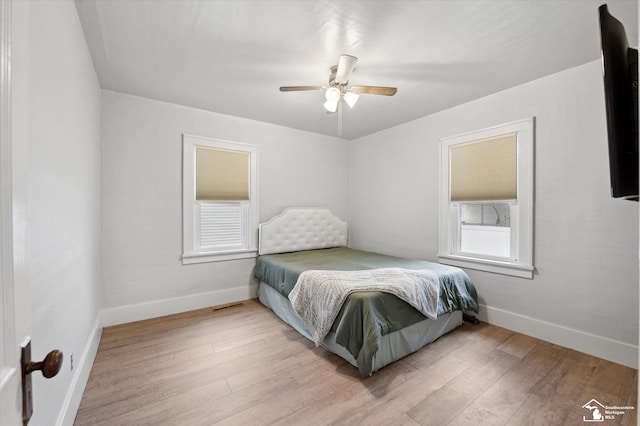 bedroom featuring a ceiling fan, visible vents, baseboards, and wood finished floors