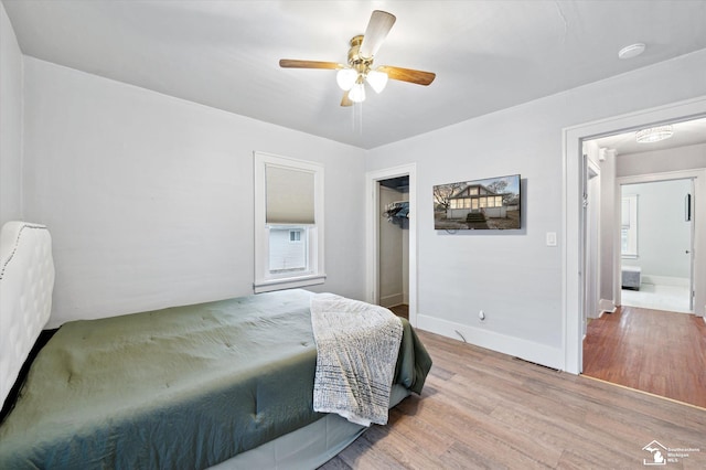 bedroom with baseboards, ceiling fan, wood finished floors, a spacious closet, and a closet