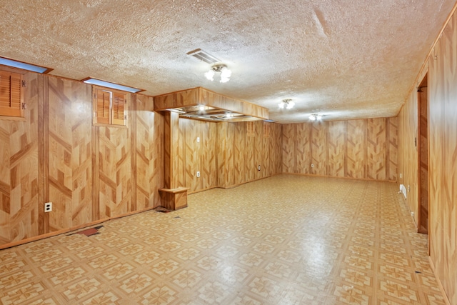 finished basement featuring wood walls, a textured ceiling, and light floors