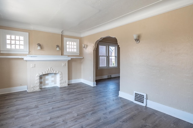 unfurnished living room featuring visible vents, baseboards, a fireplace, wood finished floors, and arched walkways