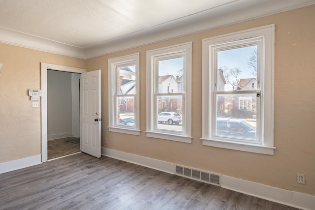 unfurnished room featuring visible vents, baseboards, and wood finished floors