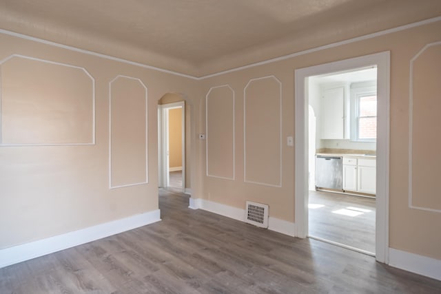 empty room featuring baseboards, wood finished floors, visible vents, and arched walkways