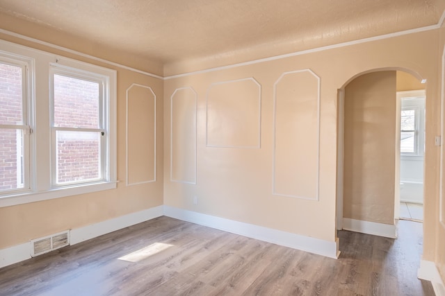 unfurnished room featuring visible vents, a textured ceiling, wood finished floors, arched walkways, and baseboards