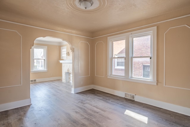 unfurnished room featuring arched walkways, visible vents, baseboards, and wood finished floors