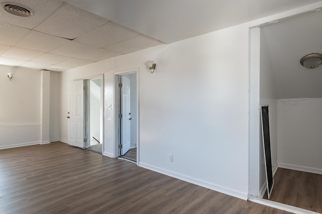 spare room featuring a drop ceiling, visible vents, baseboards, and dark wood-style flooring