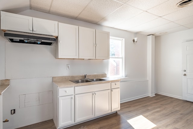 kitchen featuring a drop ceiling, light countertops, light wood-type flooring, white cabinetry, and a sink