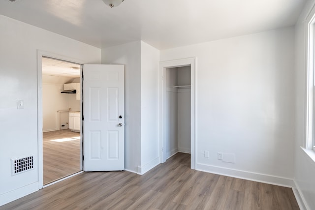 unfurnished bedroom featuring wood finished floors, visible vents, a closet, and baseboards