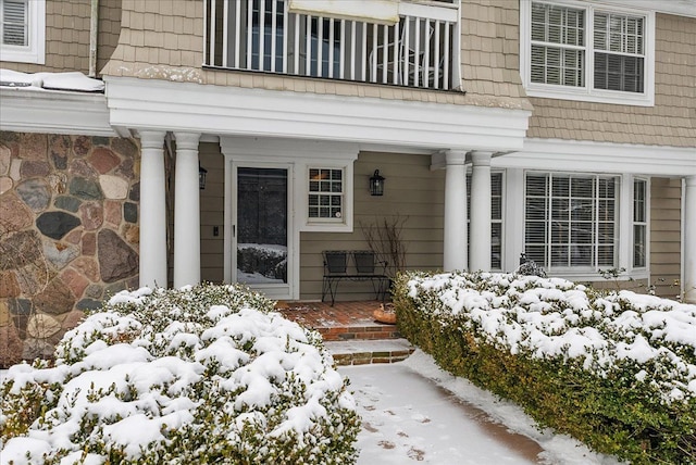 snow covered property entrance featuring a balcony, covered porch, and mansard roof