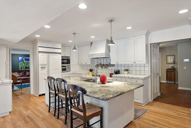 kitchen featuring built in appliances, a sink, white cabinets, and custom range hood