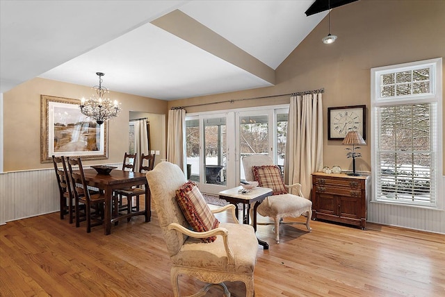 dining room with light wood-type flooring, a wainscoted wall, a notable chandelier, and lofted ceiling