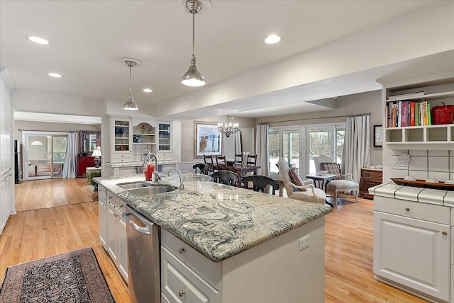 kitchen with light wood finished floors, an island with sink, stainless steel dishwasher, white cabinetry, and a sink