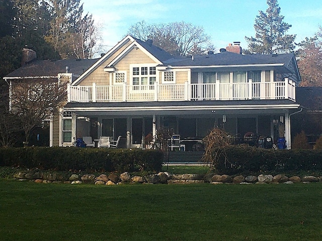 back of house with a chimney, a yard, and a balcony