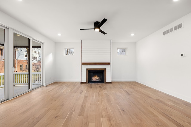 unfurnished living room with visible vents, a ceiling fan, a large fireplace, light wood-type flooring, and baseboards