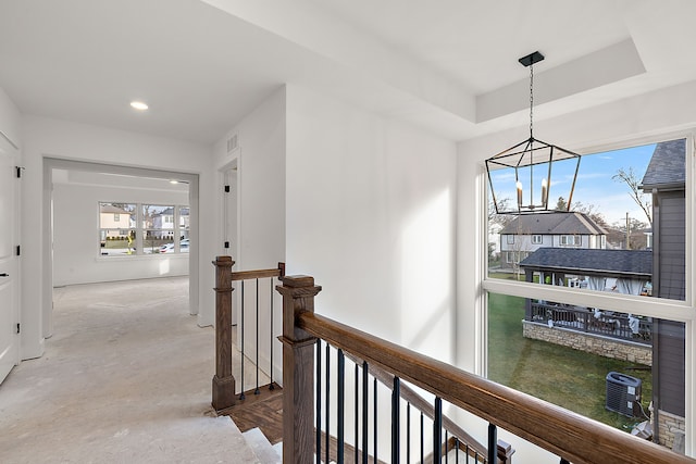 corridor with visible vents, a raised ceiling, an upstairs landing, concrete floors, and recessed lighting