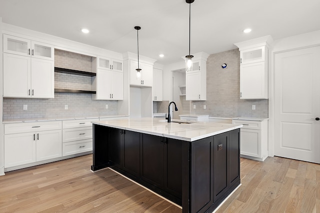 kitchen featuring open shelves, light wood-style flooring, a kitchen island with sink, white cabinets, and a sink