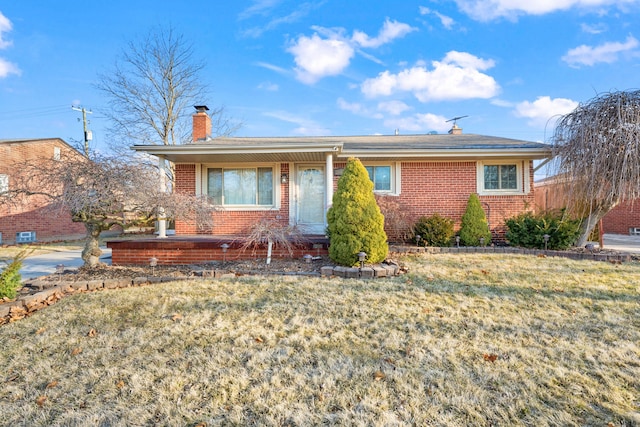 ranch-style house with brick siding, a chimney, and a front yard