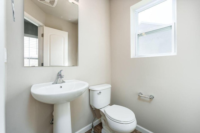 half bath with visible vents, a sink, toilet, and baseboards