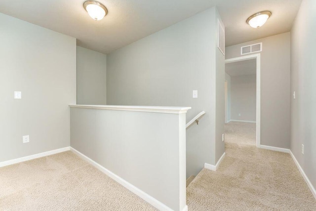 hallway featuring carpet flooring, visible vents, baseboards, and an upstairs landing