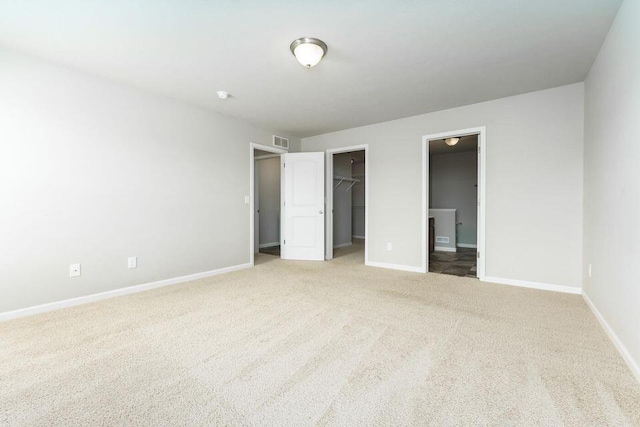 unfurnished bedroom with baseboards, visible vents, a walk in closet, carpet floors, and a closet