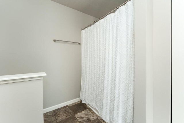 bathroom featuring stone finish flooring, curtained shower, and baseboards