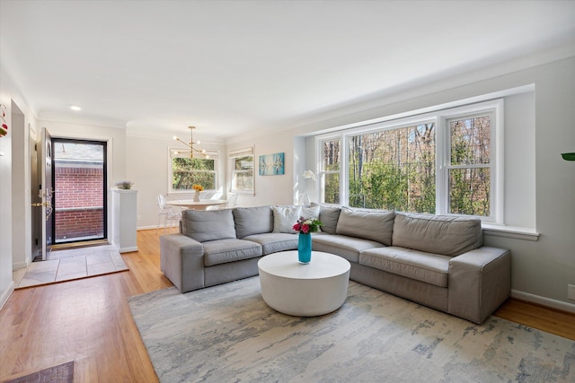 living room with light wood-type flooring, crown molding, baseboards, and a notable chandelier