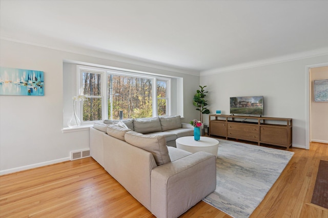 living room with light wood-type flooring, visible vents, crown molding, and baseboards