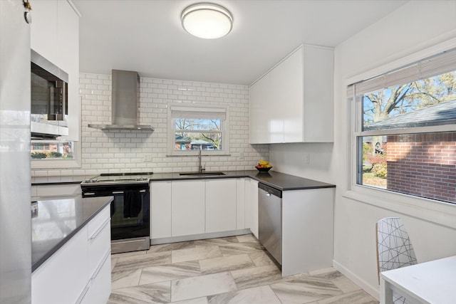 kitchen featuring stainless steel appliances, a sink, wall chimney range hood, tasteful backsplash, and dark countertops