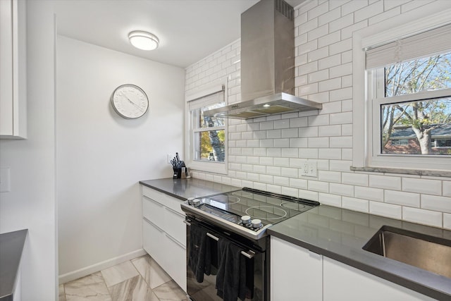 kitchen with tasteful backsplash, dark countertops, wall chimney exhaust hood, black / electric stove, and white cabinetry