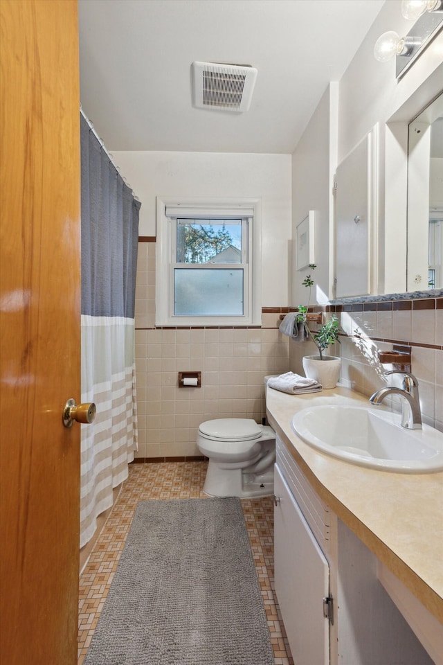 bathroom featuring visible vents, toilet, a wainscoted wall, vanity, and tile walls