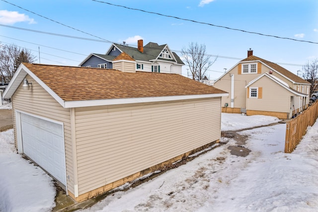 view of snowy exterior featuring roof with shingles, a detached garage, and fence