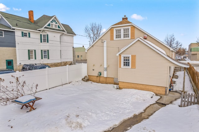 snow covered house featuring a chimney and fence