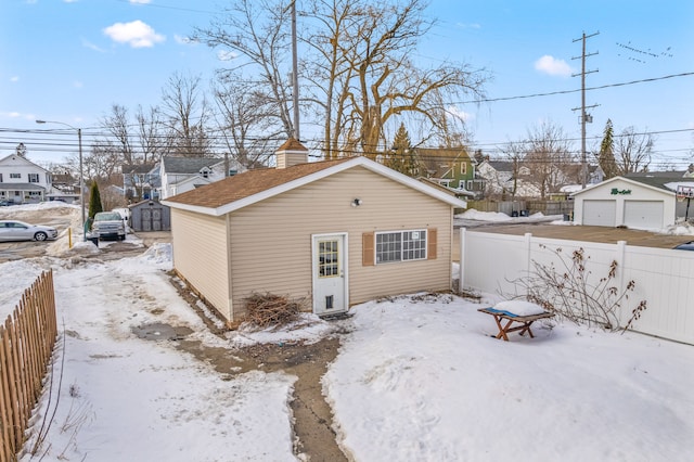 snow covered house with an outbuilding, a detached garage, fence, and a residential view