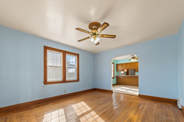 spare room featuring light wood-style floors, baseboards, arched walkways, and a ceiling fan