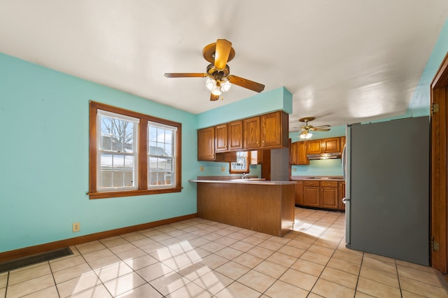 kitchen with visible vents, brown cabinets, freestanding refrigerator, a peninsula, and stovetop