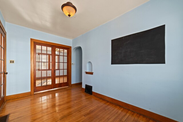 empty room featuring arched walkways, french doors, visible vents, and hardwood / wood-style floors