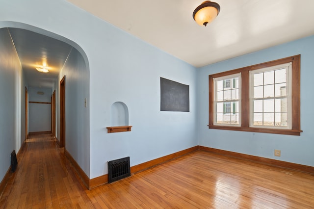 unfurnished room featuring baseboards, visible vents, arched walkways, and hardwood / wood-style floors