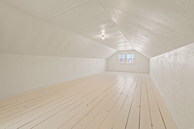 additional living space with wood-type flooring, vaulted ceiling, and a textured ceiling