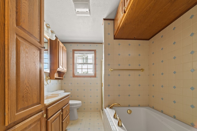 bathroom featuring tiled bath, toilet, a textured ceiling, vanity, and tile walls