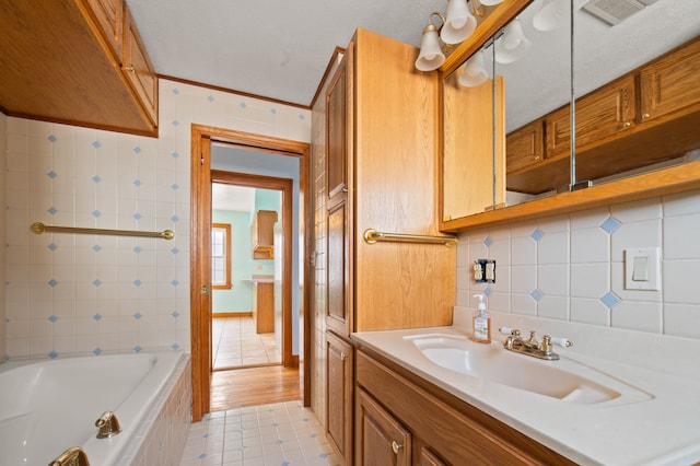 bathroom featuring crown molding, tile walls, visible vents, vanity, and tiled tub