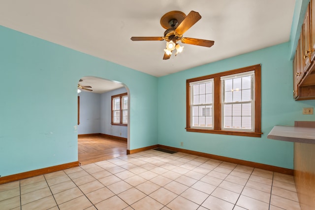 empty room with arched walkways, ceiling fan, baseboards, and light tile patterned floors