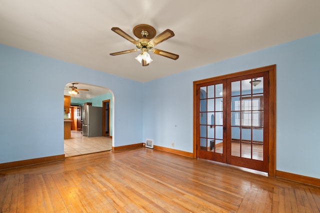 empty room featuring light wood-type flooring, baseboards, arched walkways, and french doors