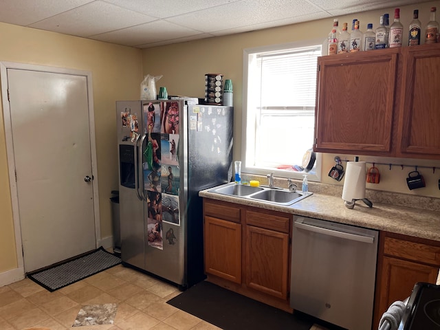 kitchen featuring appliances with stainless steel finishes, a drop ceiling, a sink, and brown cabinets